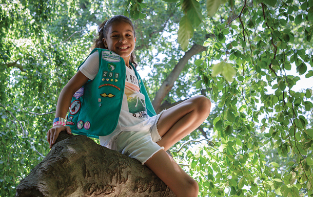 Junior Girl Scout, wearing her uniform, sitting in a tree.